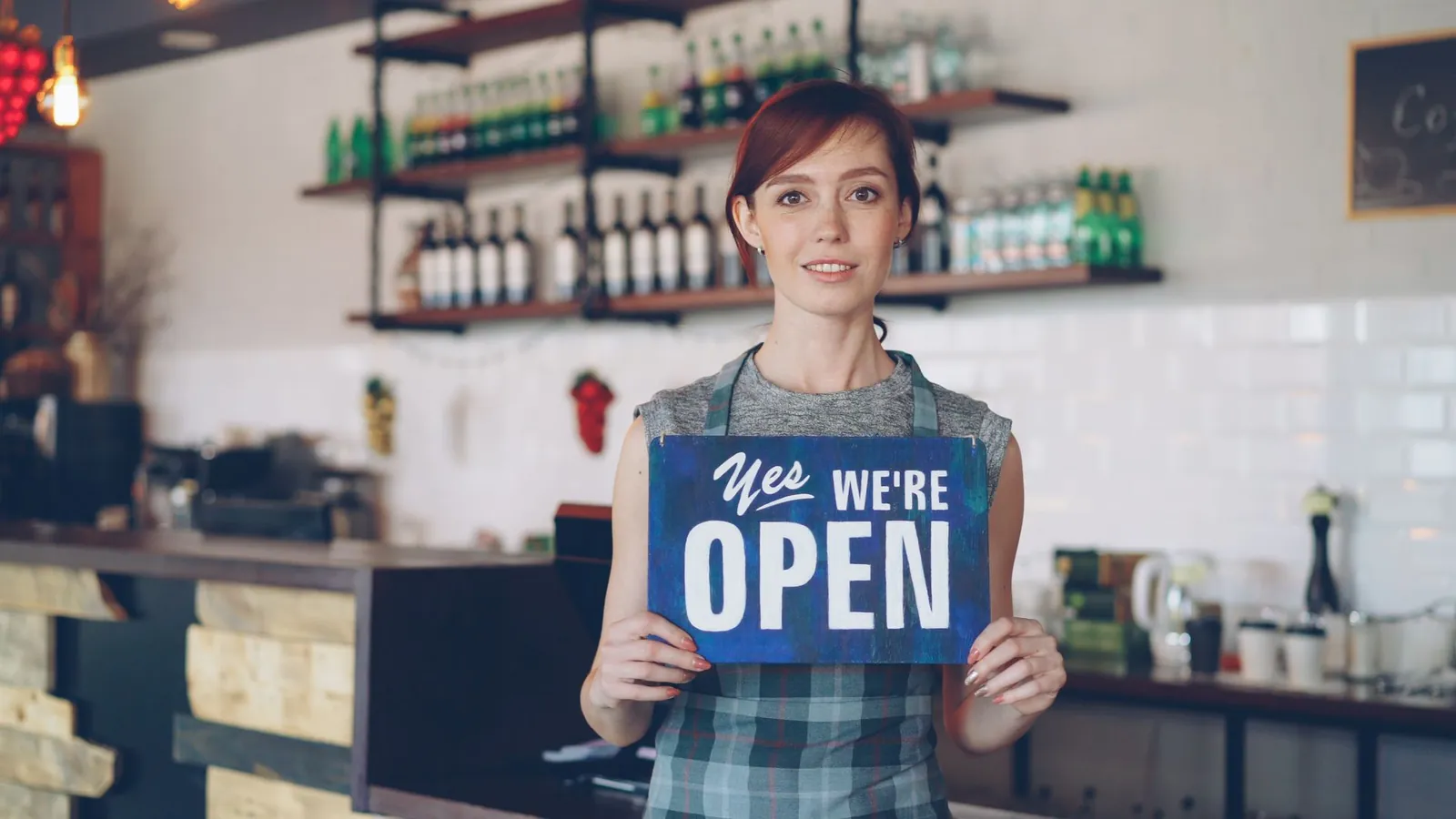 Café owner holding a 'Yes, we're open' sign behind the counter