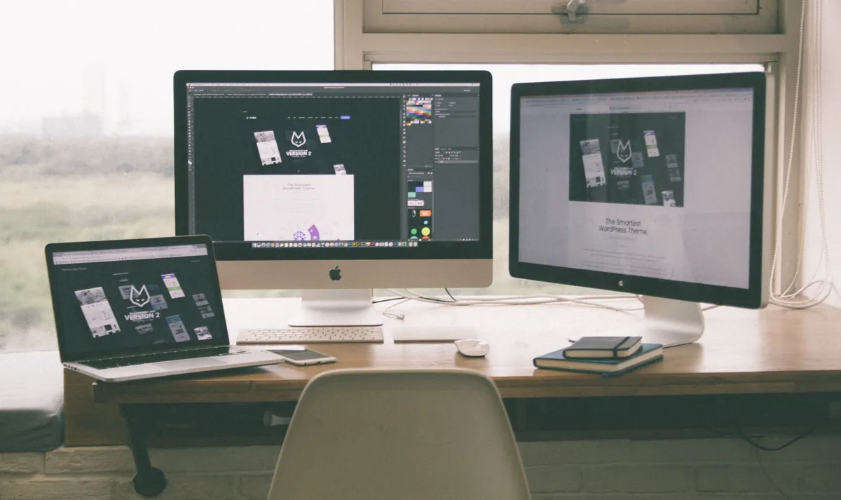 Website designs being worked on across a laptop and two desktop monitors